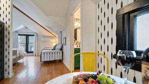 Una habitación con cama, un radiador, una mesa de comedor con fruta y vino, y vistas a una cocina.