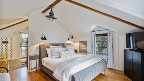 Un dormitorio con cama, mesitas de noche, televisión y ventana con cortinas.