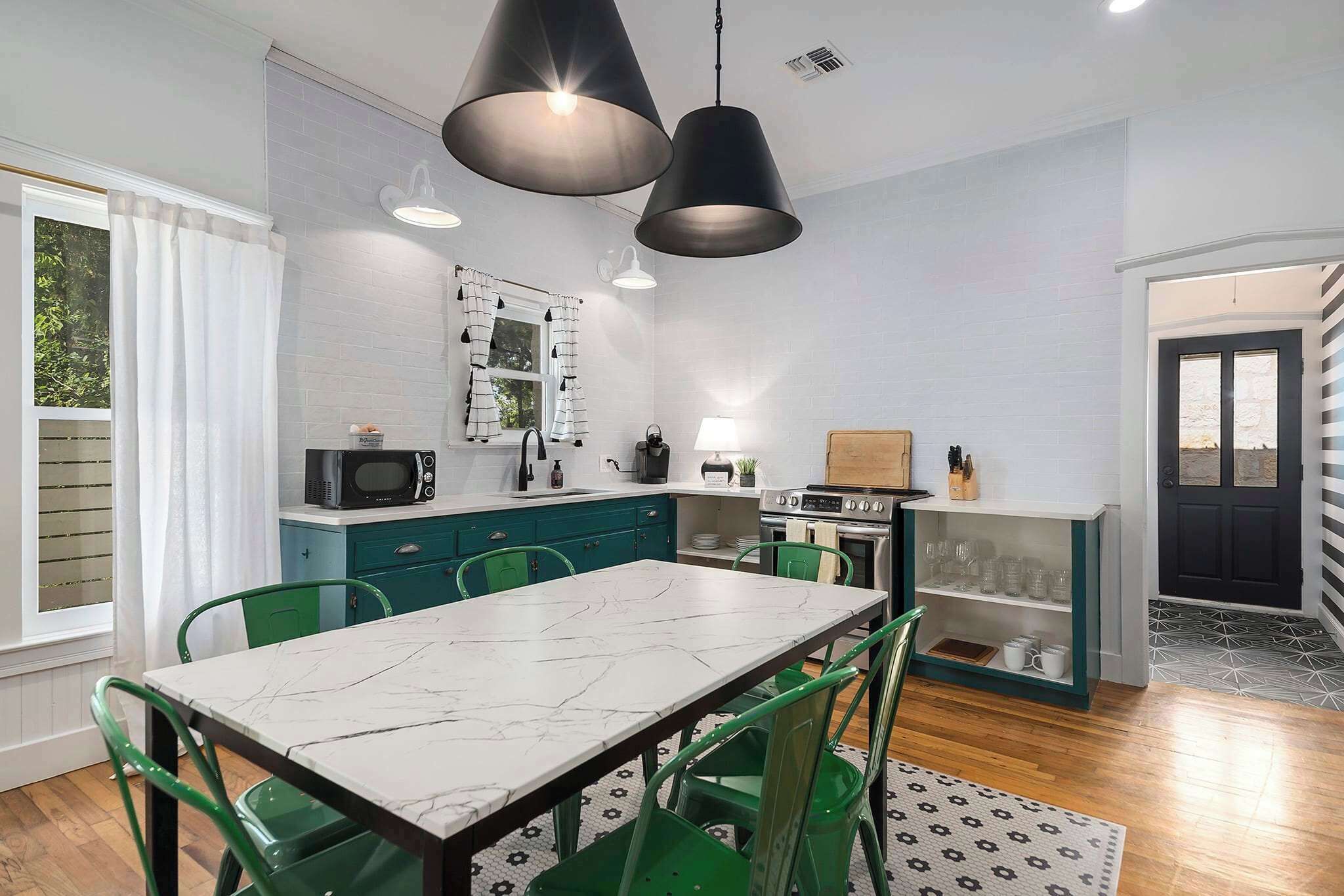 A modern kitchen with a marble countertop, green chairs, and pendant lighting.