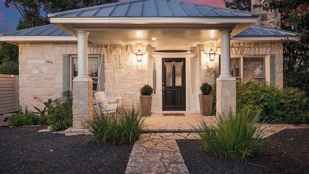A stone house with a covered porch, a black door, and a small garden with plants and a pathway. - Stonewall Main Haus - Sleeps 6 (Stonewall)