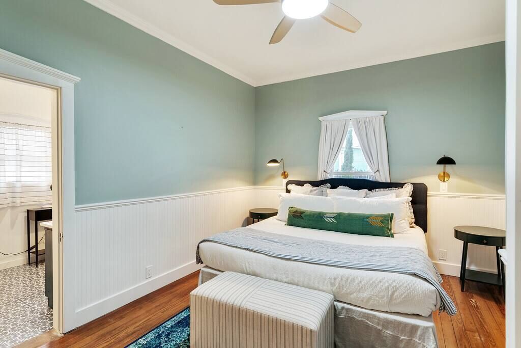 A bedroom with a bed, bedside tables, a ceiling fan, a window with curtains, and a small table by the window.