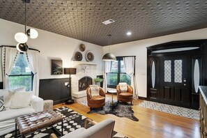 A living room with a fireplace, leather armchairs, a white sofa, a patterned rug, and a black door.