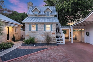 A stone house with a metal roof, a brick pathway, and a staircase leading to a covered area.
