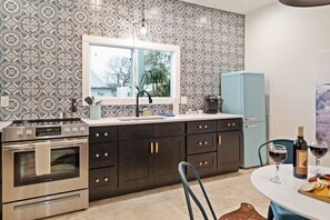 A kitchen with patterned wallpaper, a window, a stove, a refrigerator, and a dining area with a table set for two.