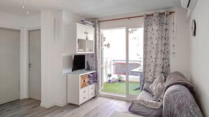 A living room with a sofa, a TV on a stand, a sliding glass door to a balcony, and a white cabinet with shelves. - Awesome apartment in Puerto de Mazarron (Puerto de Mazarron)