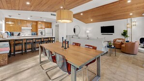 Een moderne keuken met houten kasten, een eettafel en een aan de muur bevestigde televisie.