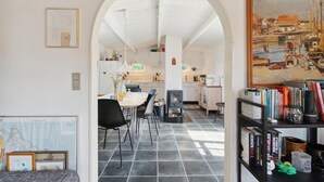 Moderni keittiö, jossa on valkoiset kaapit, ruokailutila mustilla tuoleilla ja täynnä kirjoja oleva kirjahylly.