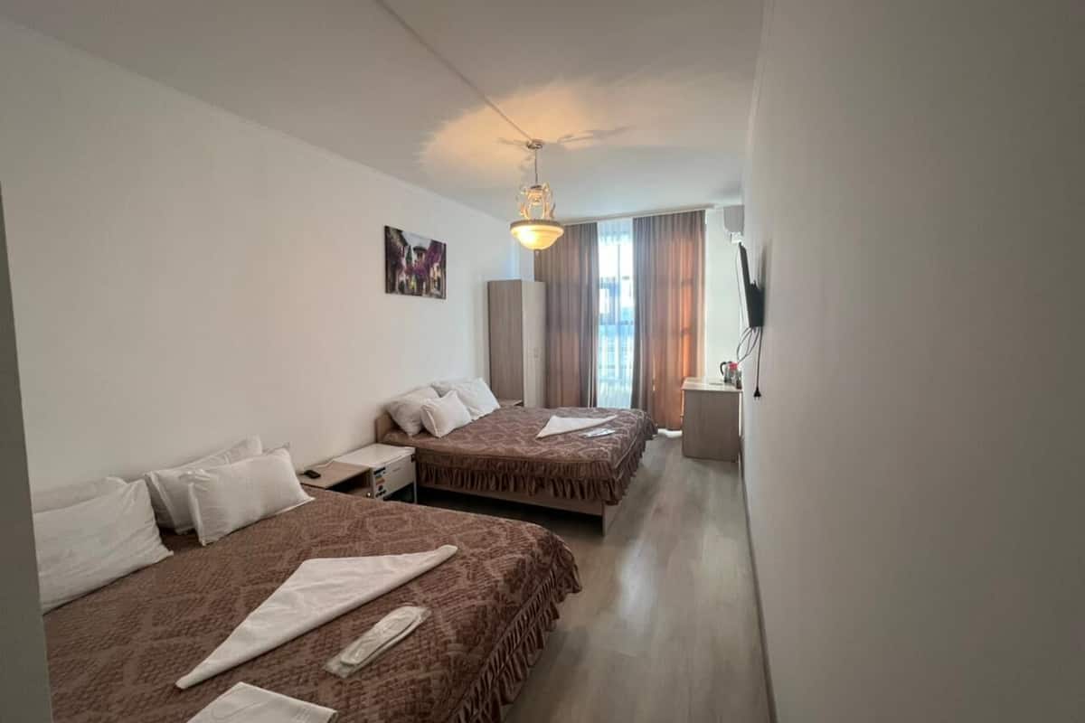 A hotel room with two beds, a desk, a chair, a lamp, and a window with curtains.