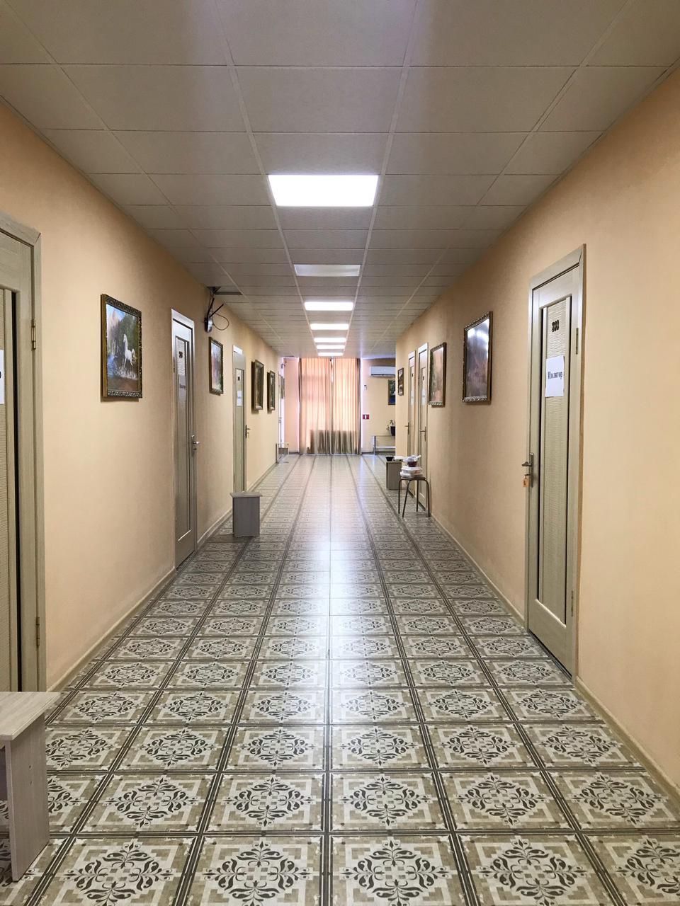 Ein Hotelkorridor mit gemusterten Bodenfliesen, Türen und gerahmten Bildern an den Wänden.