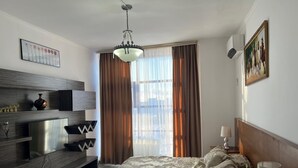 A hotel room with a bed, a TV, a desk, and a window with curtains. - Zeraviktoria (Atyrau)