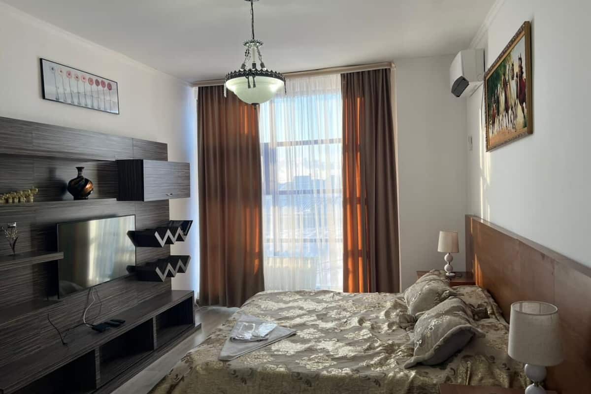 A hotel room with a bed, a TV, a desk, and a window with curtains.