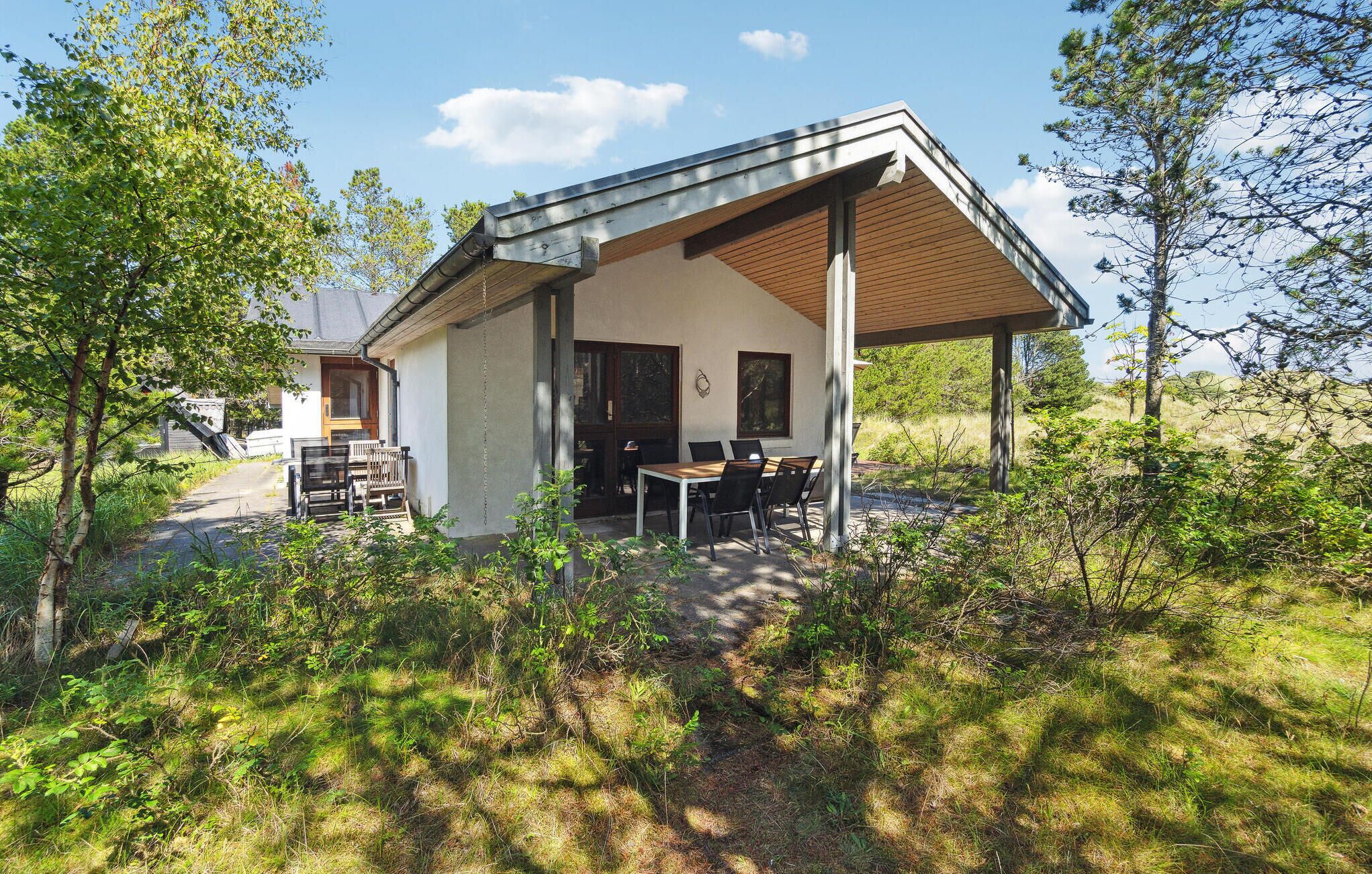 A modern building with a covered patio, a dining area with tables and chairs, and a view of the surrounding forest.