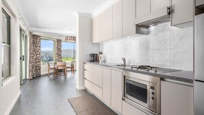 Eine moderne Küche mit Einbauofen, Gasherd und Mikrowelle. Es gibt einen Essbereich mit Tisch und Stühlen sowie einen Blick ins Freie durch ein großes Fenster.
