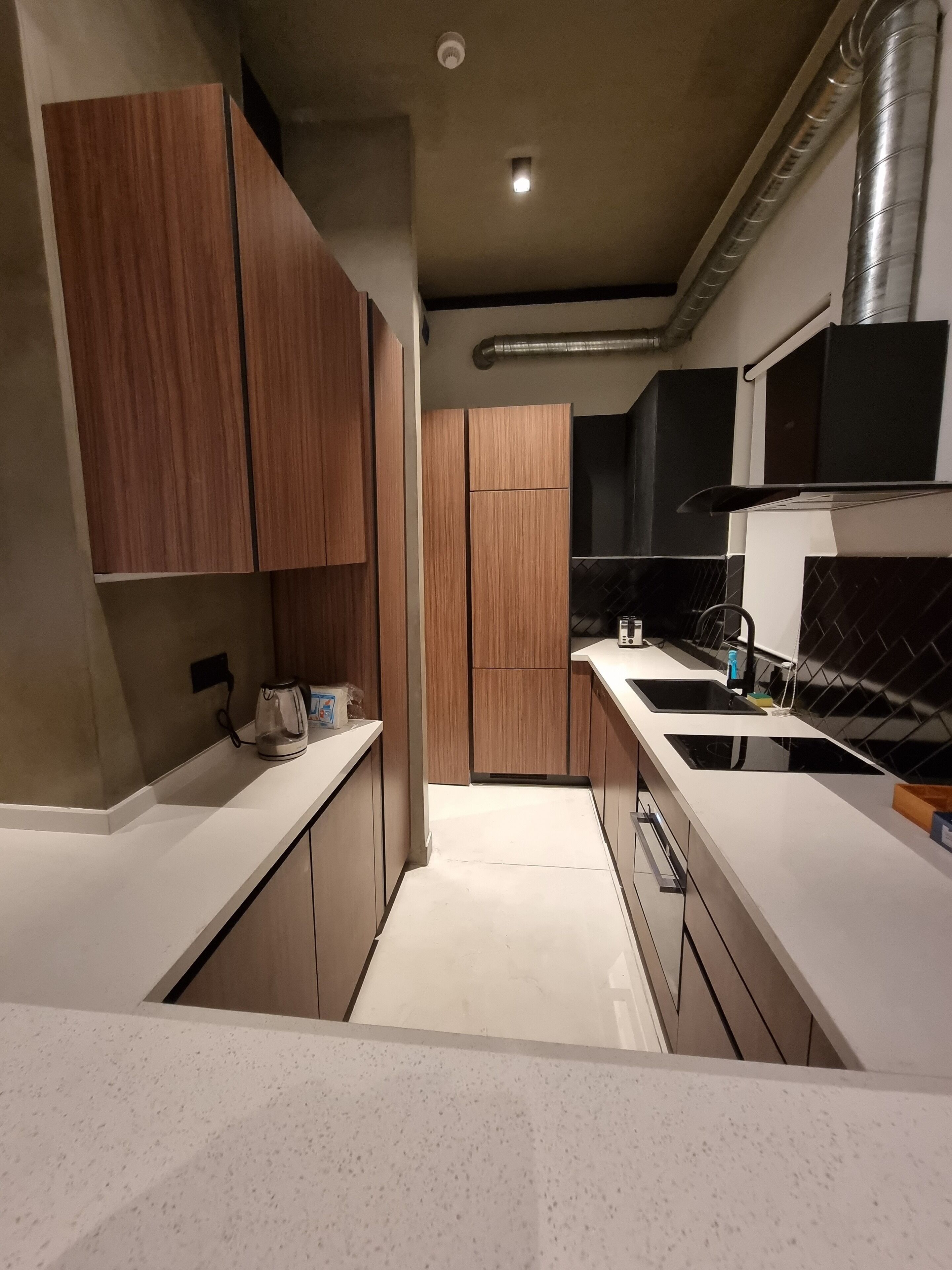 Een moderne keuken met houten kastjes, een wit aanrecht en een zwarte achterwand.