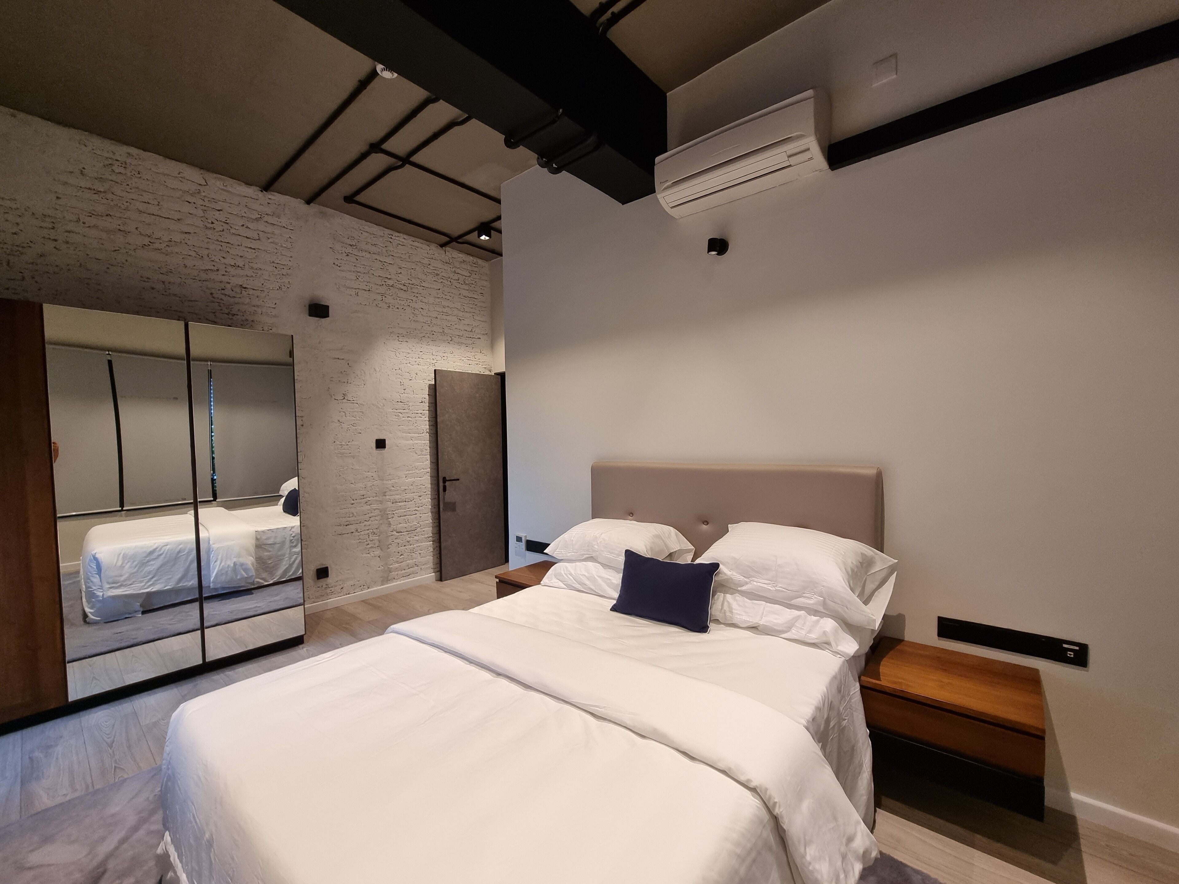 A modern bedroom with a large bed, a wardrobe with mirrors, and an air conditioning unit on the ceiling.
