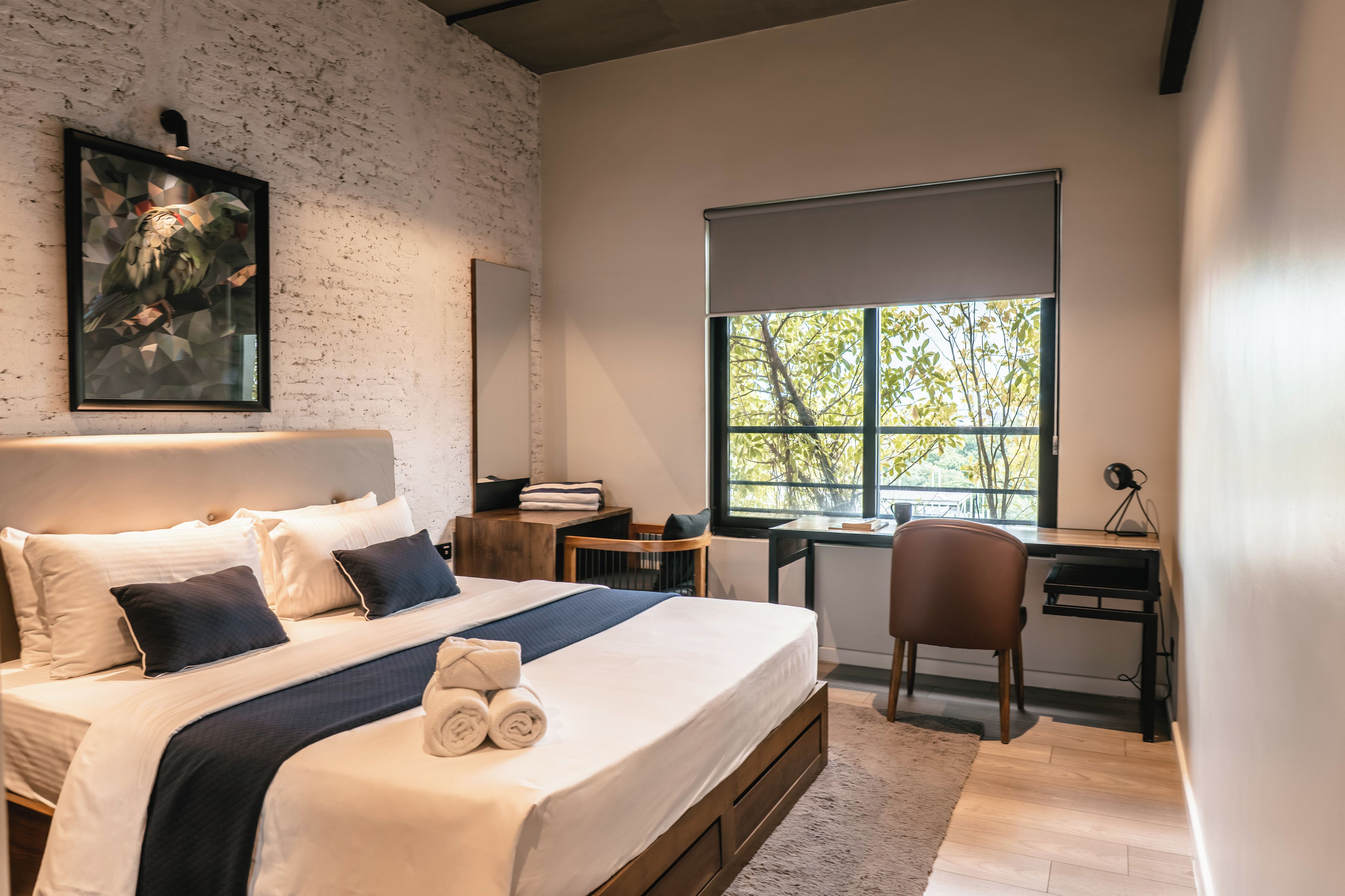 Un dormitorio moderno con una cama grande, un escritorio y un ventanal con vistas a árboles.