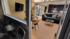 Ett modernt vardagsrum med en soffa, ett soffbord och stolar. En tv är monterad på väggen och i bakgrunden syns ett köksområde.
