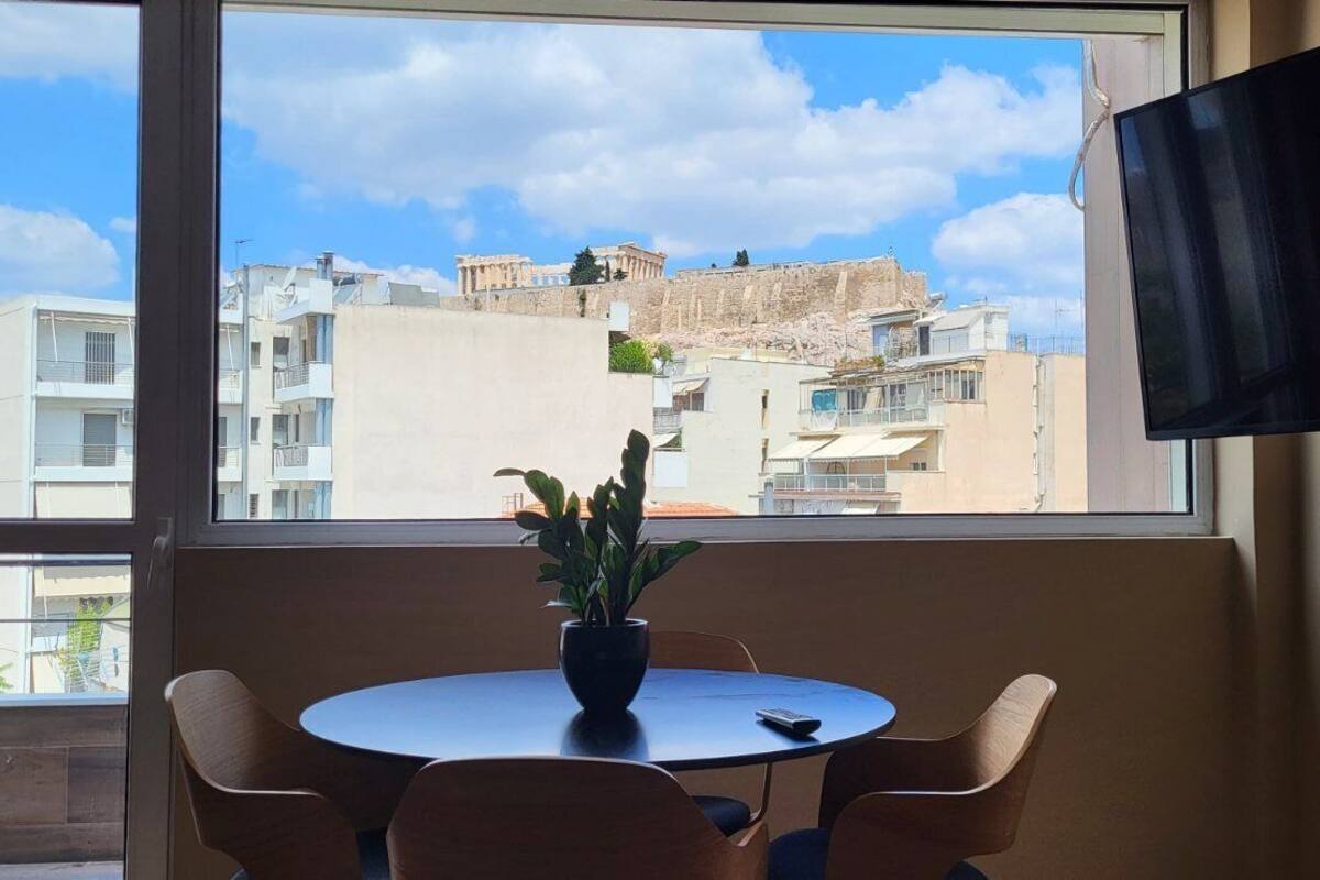 A room with a large window offering a view of ancient ruins and modern buildings.