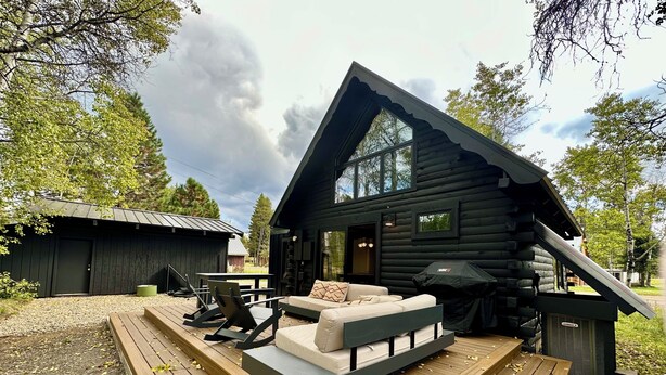 Une cabane en rondins dotée d’une terrasse, de meubles de jardin et d’une grande fenêtre.