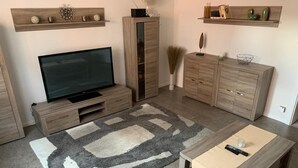 A modern living room with a flat-screen TV, wooden cabinets, a coffee table, and a patterned rug.
