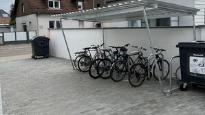 Zona techada para estacionamiento de bicicletas con un bote de basura y un contenedor para reciclaje.