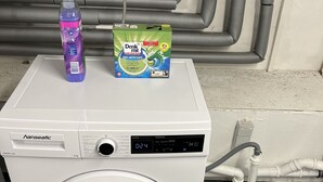 Lavadora de carga frontal con pantalla digital, una botella de detergente y una caja de polvo para ropa en la parte superior.