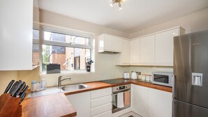 A modern kitchen with white cabinets, stainless steel appliances, a wooden countertop, and a window providing natural light. - Stunning 2-bed Apartment in Windsor - Free Parking (Windsor)