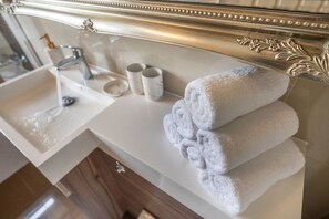 A bathroom with a sink, faucet, and two rolled towels on a white countertop.