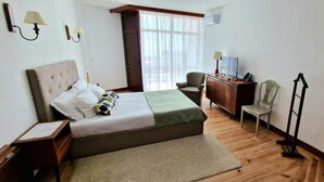 A bedroom with a bed, a desk, a chair, a dresser, and a window with curtains.