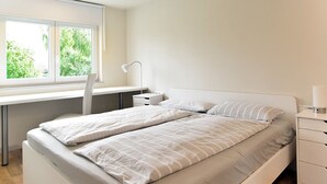 A bedroom with a bed, a desk, and a window.