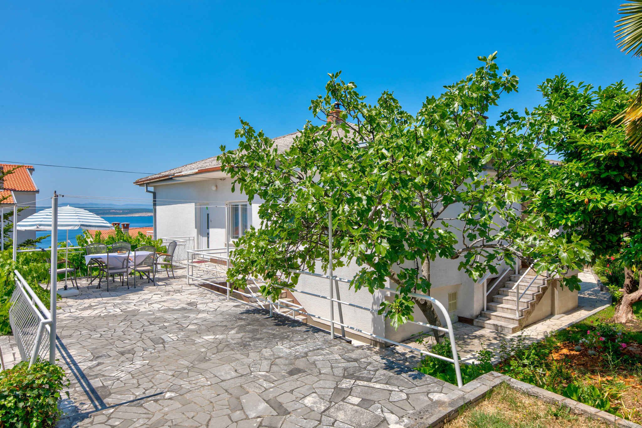 A patio with stone flooring, a table and chairs, a staircase, and a view of the sea.