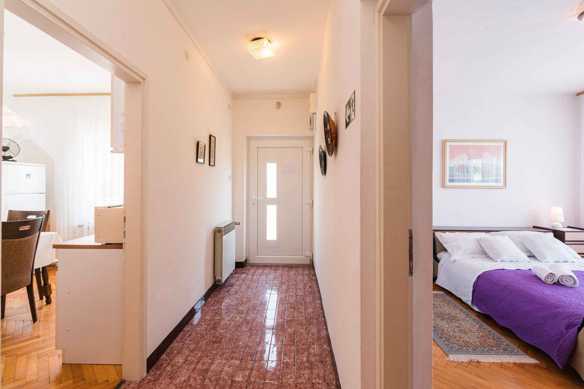 Ein Flur, der zu einem Schlafzimmer mit Bett, Heizkörper und Tür führt.