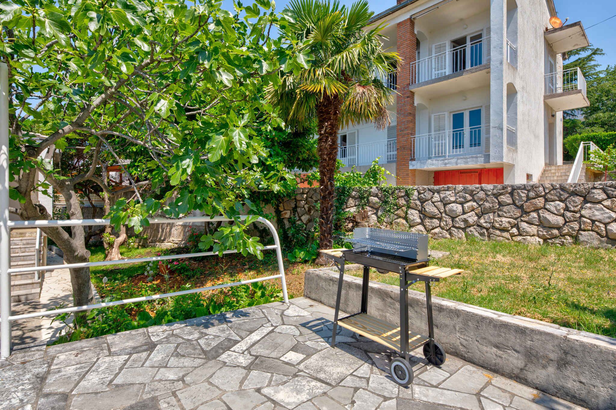 Eine Terrasse mit Grill, Steinmauer und einem Gebäude mit Balkonen.