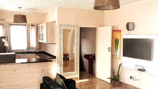 A modern living room with a sofa, a TV, and a kitchen area with a sink and cabinets. - Stunning 3-bed House in Harare (Harare)