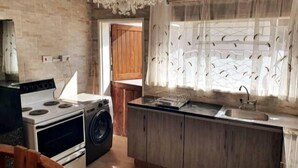 A compact kitchen with a stove, washing machine, and a window with decorative curtains. - Stunning 3-bed House in Harare (Harare)
