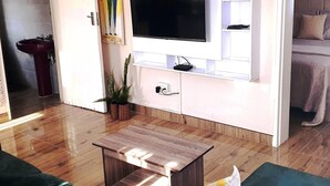 A modern living room with a flat-screen TV mounted on a white wall, a wooden coffee table, and a potted plant. - Stunning 3-bed House in Harare (Harare)