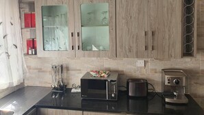 A modern kitchen with a microwave, toaster, and coffee maker on the counter. There are cabinets with glass doors and a chandelier above. - Stunning 3-bed House in Harare (Harare)