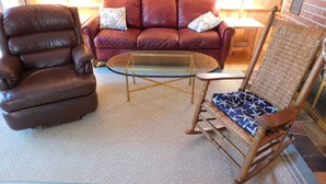 Un salon avec un canapé en cuir marron, une table basse en verre et un fauteuil à bascule en bois.