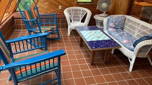 Une pièce chaleureuse aux murs en bois, avec une table à carreaux, des meubles en osier bleu et blanc et un ventilateur.
