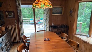 Une table à manger en bois avec des chaises, une lampe en vitrail et une vue sur l’extérieur.