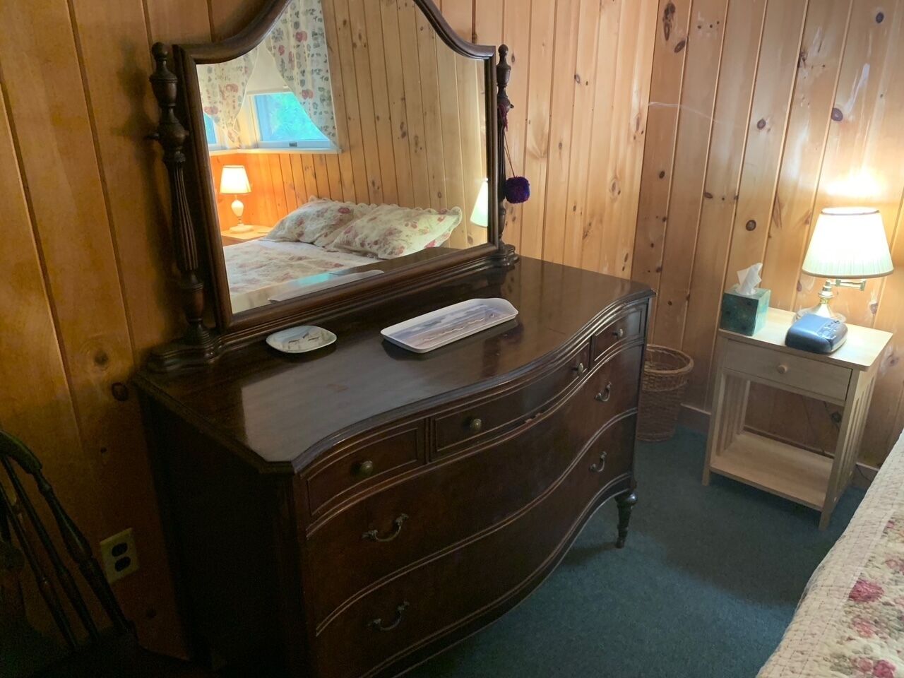 A wooden dresser with a mirror, a keyboard, and a lamp on a bedside table.