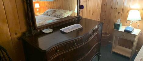A wooden dresser with a mirror, a keyboard, and a lamp on a bedside table.