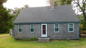 A small, single-story house with a gray shingled roof and a white door. - Path to Pond, Private Location, Sweet Home! (CS0031) (Wellfleet)
