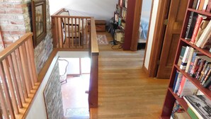 A wooden staircase leading to a lower level with a brick wall and a bookshelf filled with books. - Path to Pond, Private Location, Sweet Home! (CS0031) (Wellfleet)