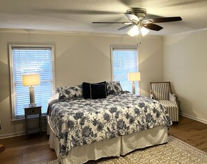 Relax in this serene bedroom with a large bed, ceiling fan, and comfortable chair.