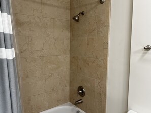 Shower area features a wall-mounted showerhead, handheld showerhead, and control knob.