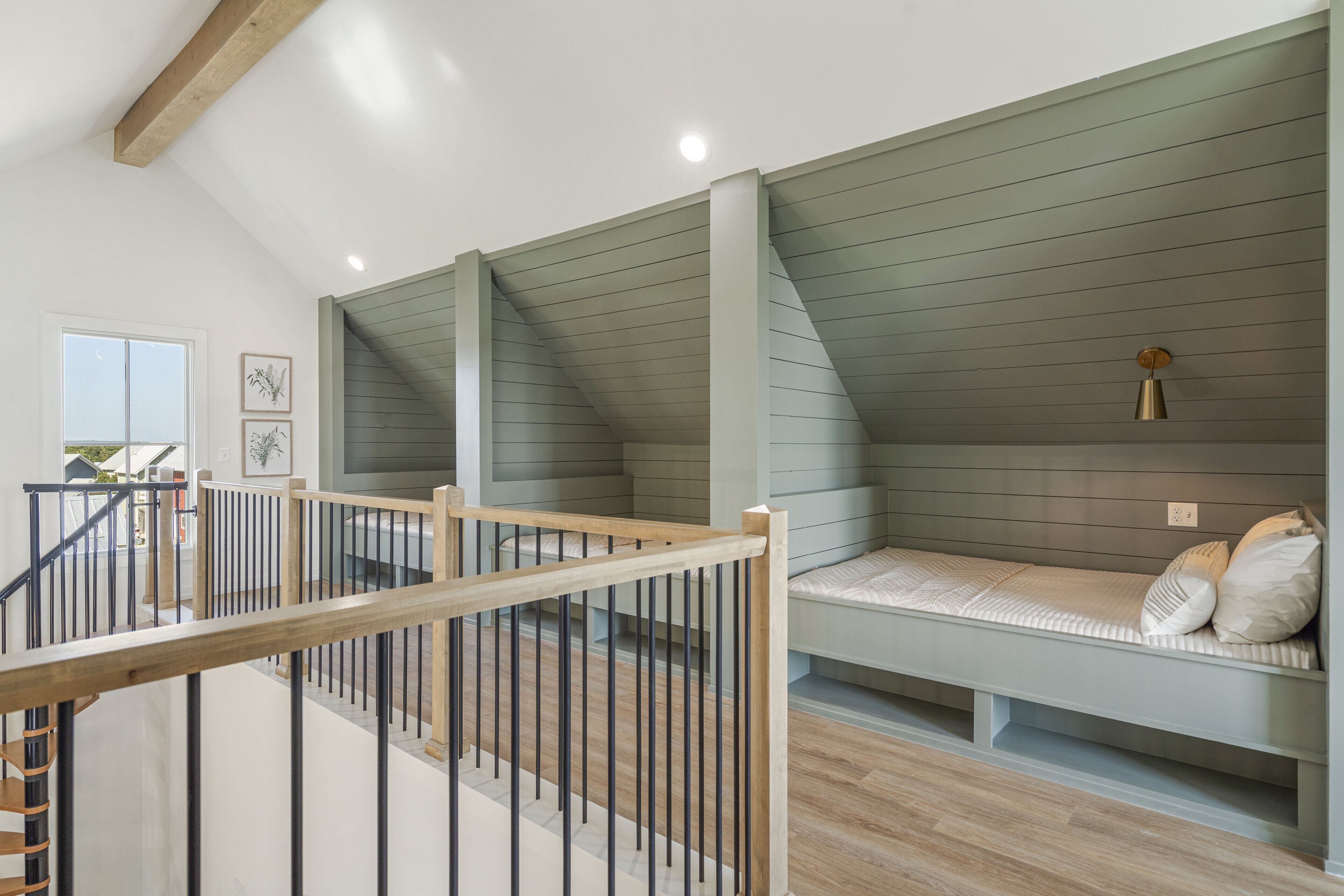 A modern loft bedroom with a sloped ceiling, a built-in bench with pillows, a wooden staircase, and a view of the outdoors.