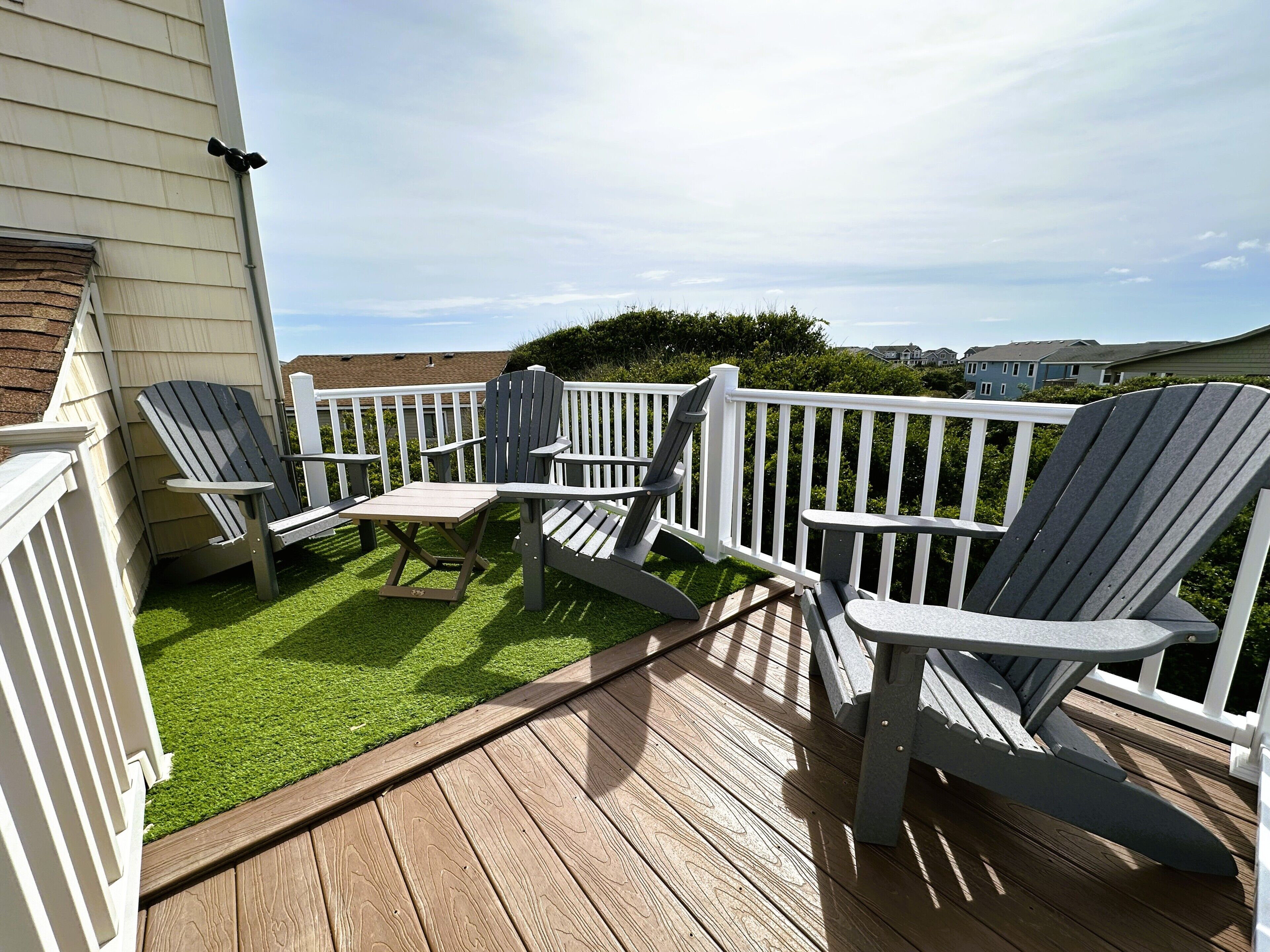 A deck with Adirondack chairs and a small table, surrounded by a white railing.
