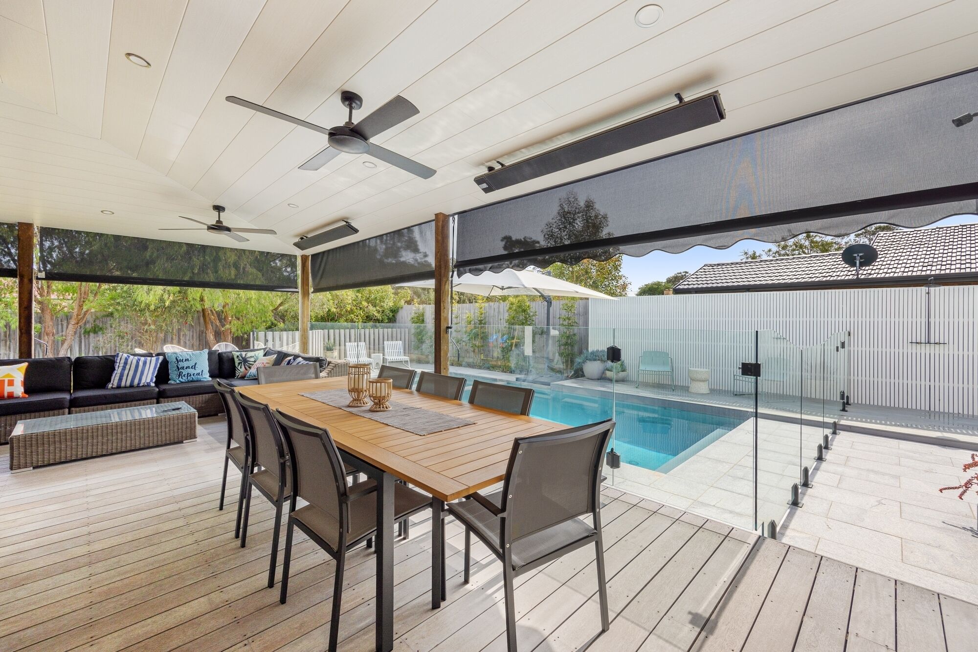 Eine Außenpatio mit Pool, Holzterrasse und einer überdachten Sitzgelegenheit mit Tisch und Stühlen.