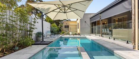 A rectangular swimming pool with a tiled deck, surrounded by a fence and potted plants.